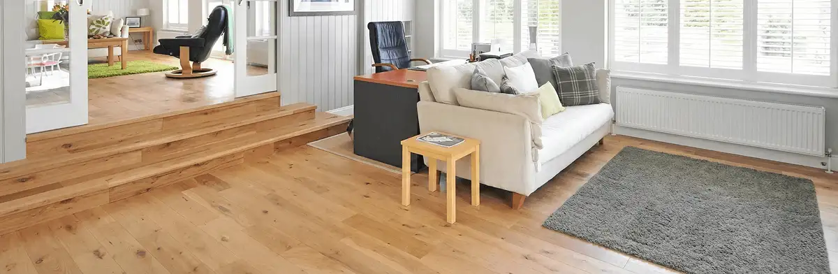 A modern living room with professionally installed laminate flooring, a beige sofa, a small side table, a gray rug, and large windows with white shutters in Charleston, SC